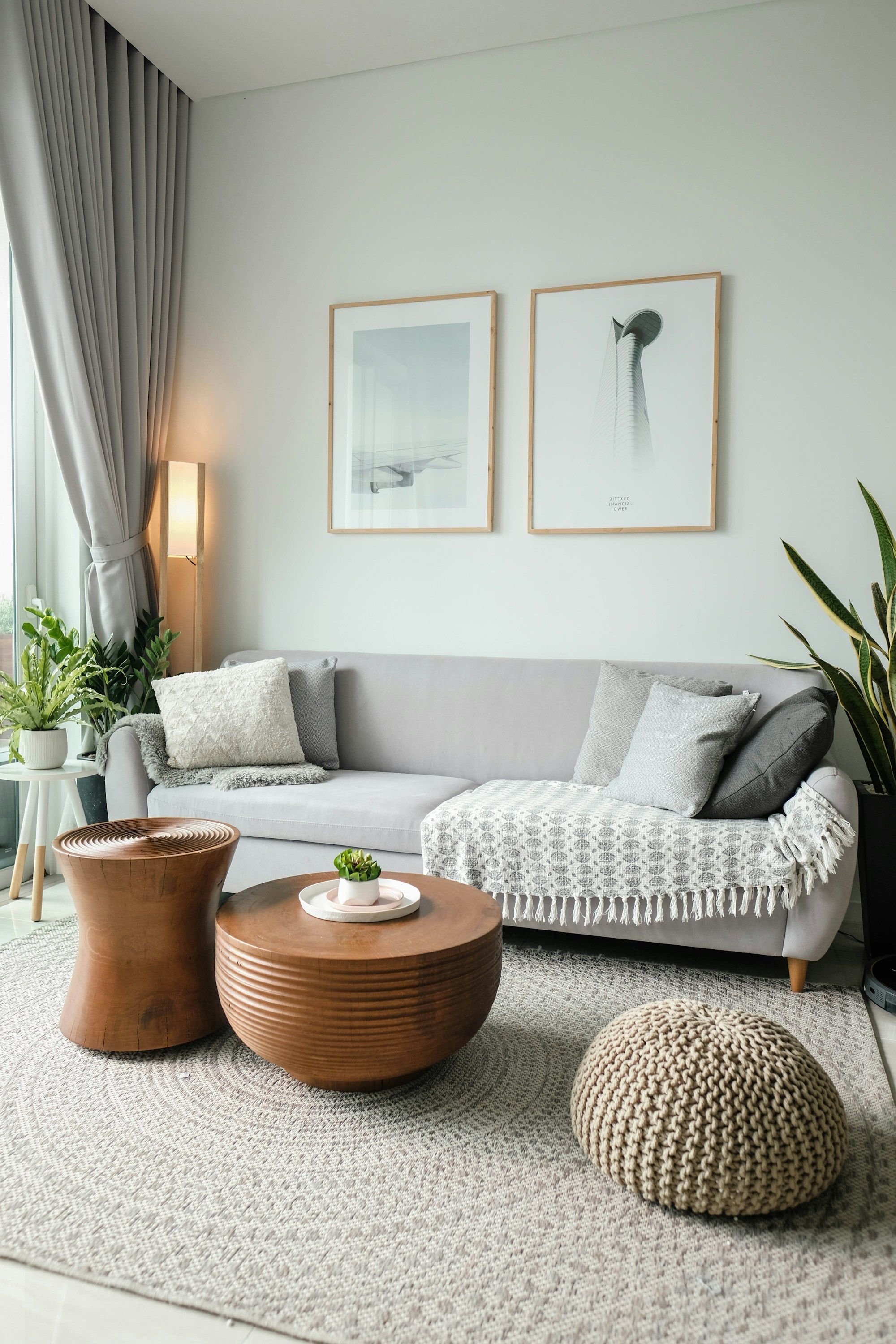 Ljust vardagsrum med grå soffa, inramade tavlor och runda soffbord i trä